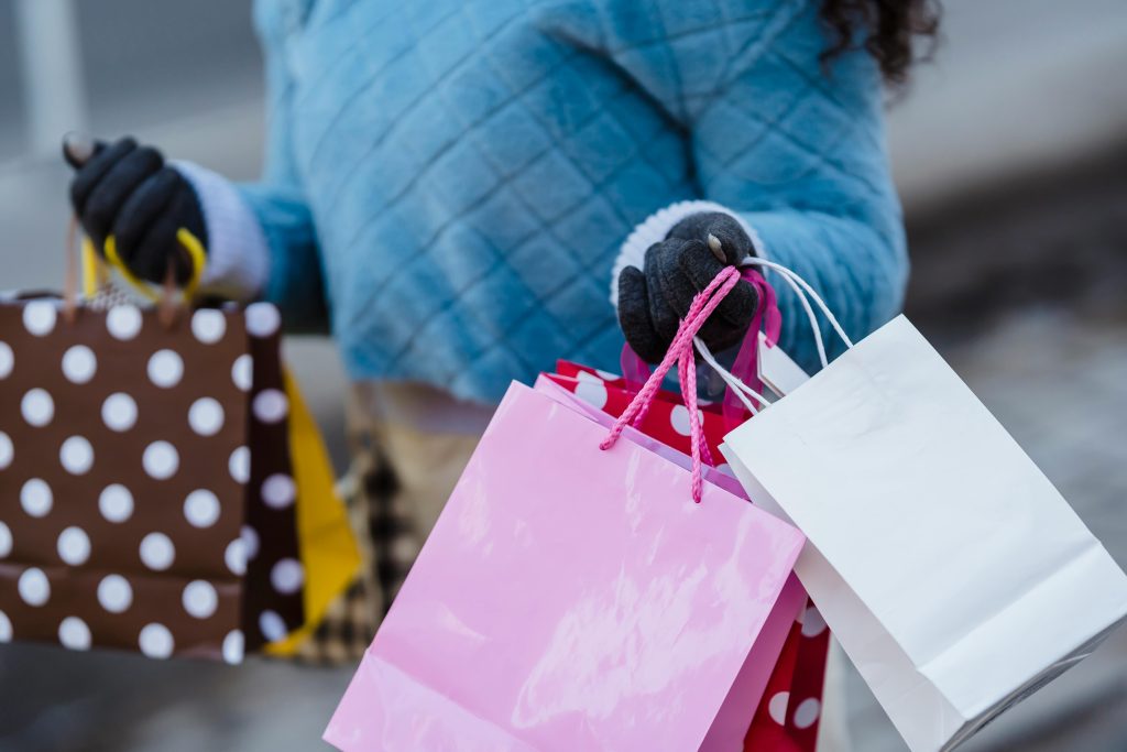 Crop anonymous female in blue soft sweater with many different colorful gift bags on blurred background